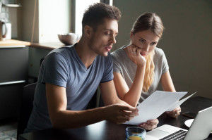 Serious young couple checking documents with using laptop